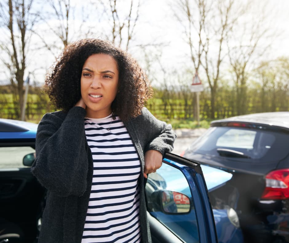 woman with subtle injury holding her neck in pain as she exits her car, which has collided with another car